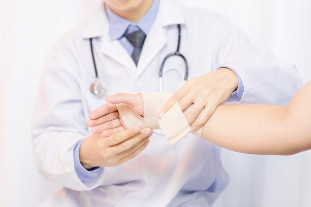 9. Cand trebuie sa mergi la medic (cadru medical care panseaza un pacient, arsura electrica la mana, ajutor specializat, fundal alb)