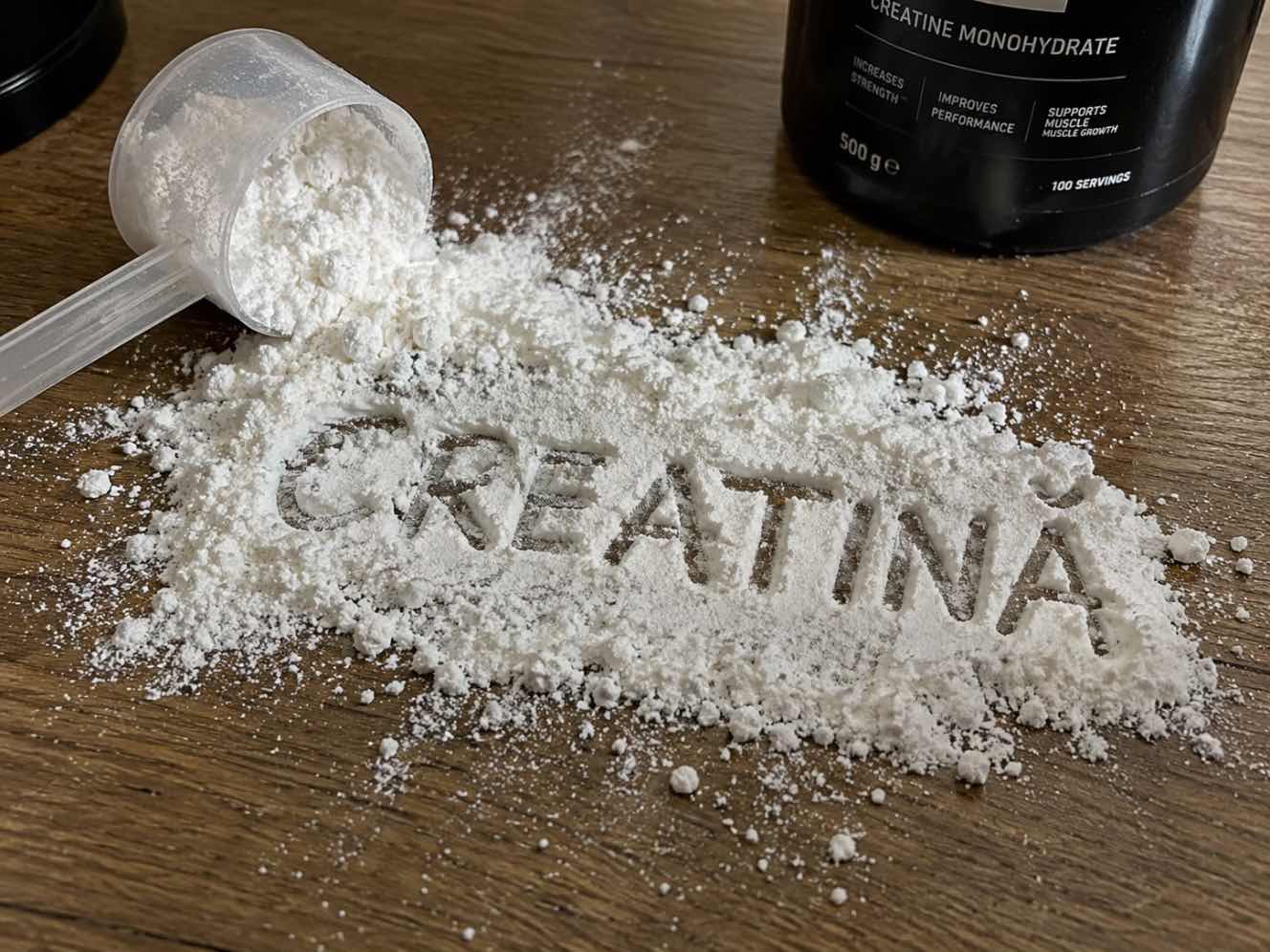 Ce riscuri poate avea creatina (cupa cu creatina varsata, supliment pentru sustinerea fortei, masa din lemn)