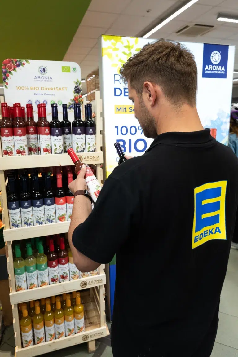 Angajat EDEKA verificând sucurile Aronia Charlottenburg la raftul din München